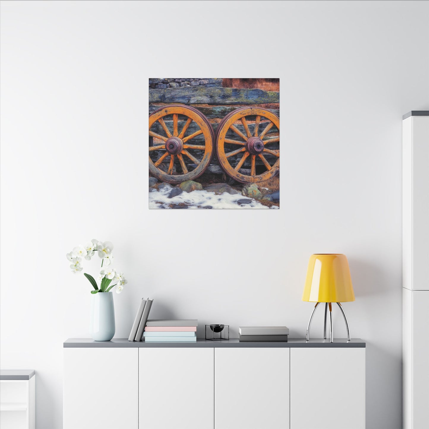 Second alternate room view. Canvas print featuring two antique wooden wagon wheels leaning against a rustic fence, with snow and stone in the foreground and rich textures throughout.