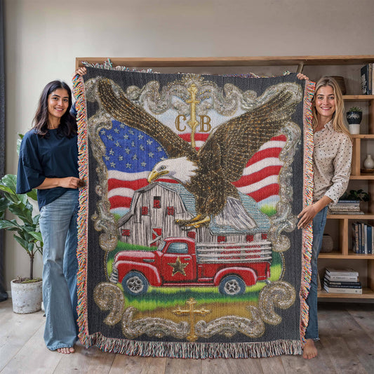 Large size, in use. Heirloom woven blanket with bald eagle, American flag, red farm truck, rustic barn, golden crosses, and customizable initials in upper center. Embroidered-style patriotic design.