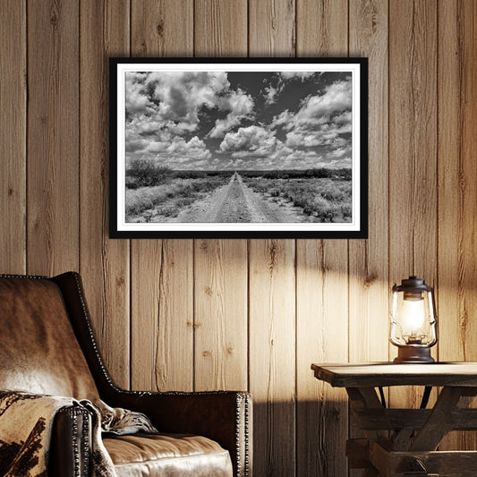 Black frame shown in room. Black and white photo of a dirt road in Texas stretching to the horizon under dramatic clouds, fine art framed landscape print.