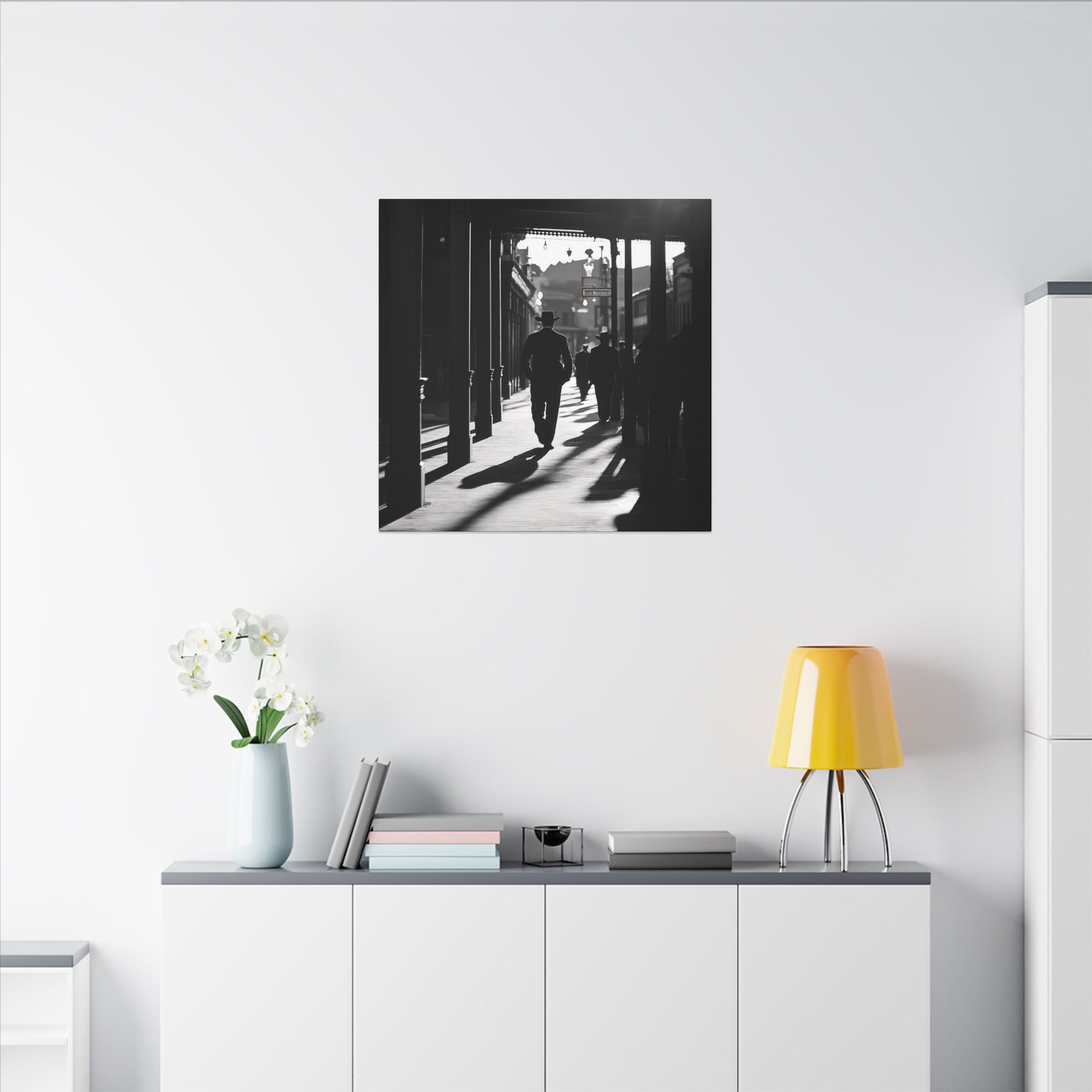 Monochromatic room. Canvas print of a silhouetted cowboy walking down a wooden sidewalk in a Western town, with long shadows and dramatic black-and-white lighting.