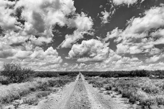 Black and white photo of a dirt road in Texas stretching to the horizon under dramatic clouds, fine art framed landscape print.