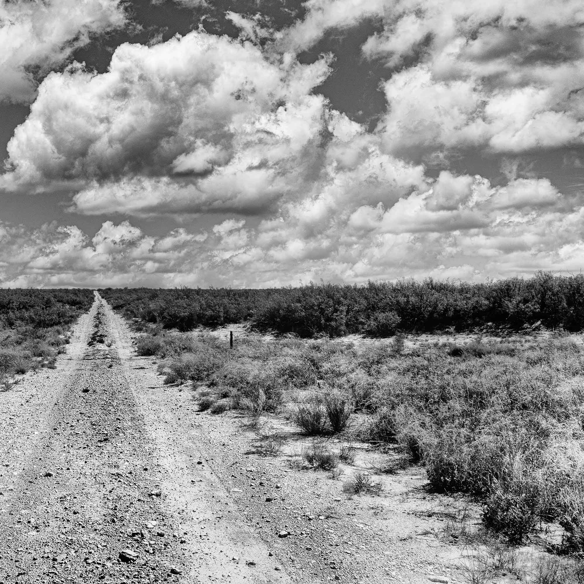 Texas dirt road stretching into the distance under dramatic clouds, black and white photograph