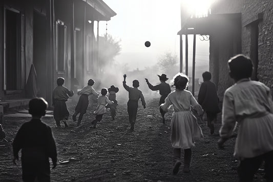 Black-and-white western street scene canvas print of children running and playing ball at sunset, capturing joyful movement and nostalgic charm. Stretched canvas art.